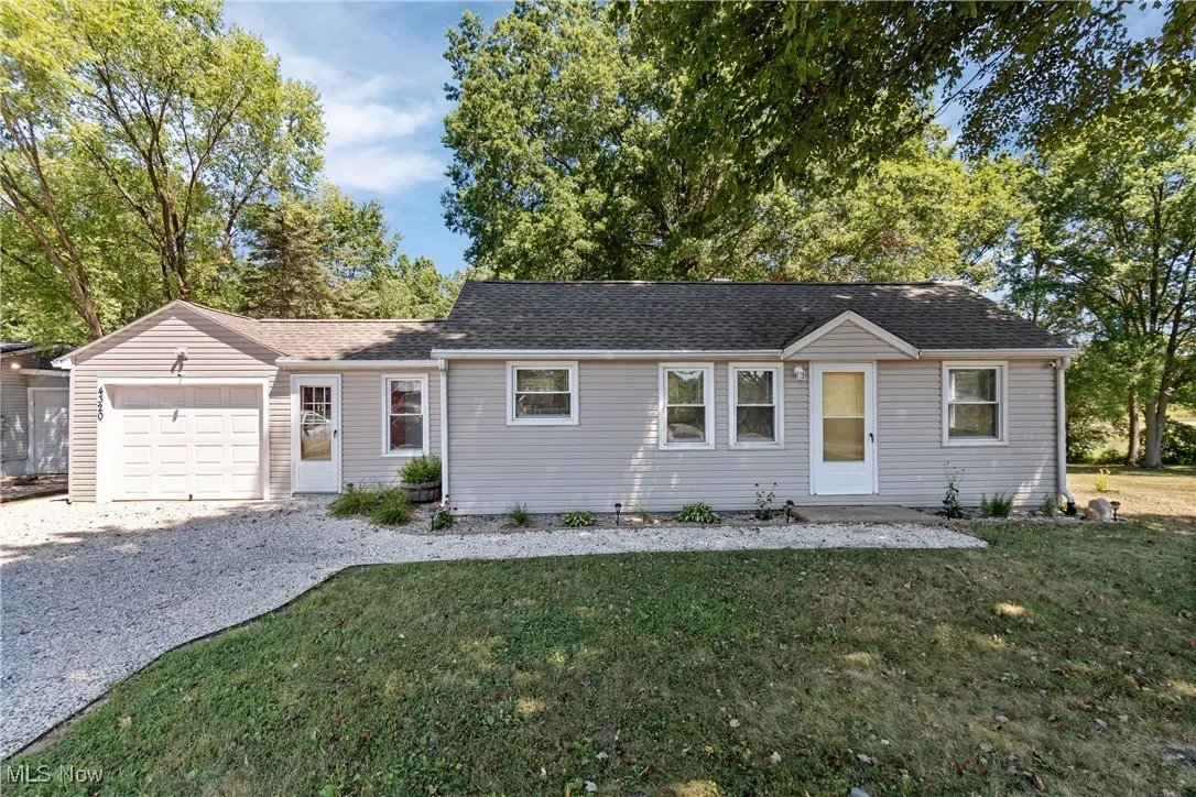 Ranch-style house with an attached garage, gravel driveway, a front lawn, and roof with shingles