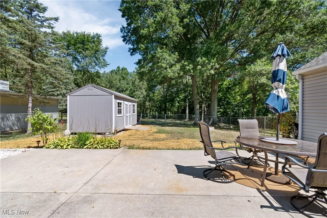 Fenced backyard with an outbuilding, outdoor dining space, a patio, and view of wooded area