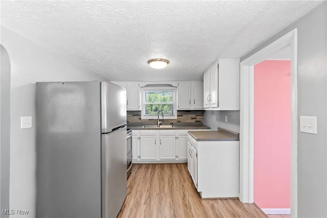 Kitchen with appliances with stainless steel finishes, white cabinetry, light wood finished floors, backsplash, and dark countertops