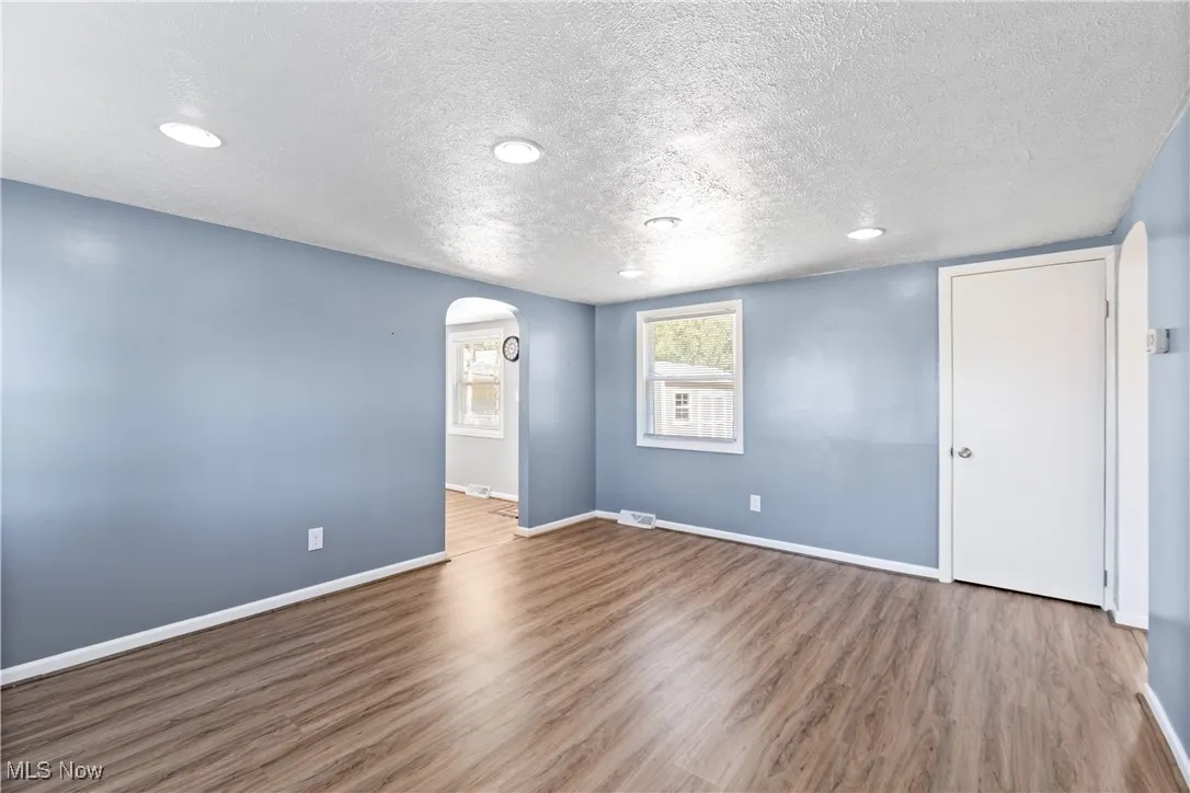 Empty room with arched walkways, wood finished floors, a textured ceiling, and recessed lighting