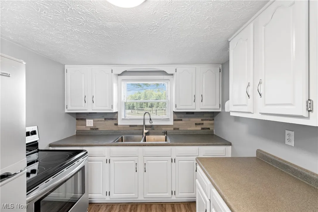 Kitchen featuring stainless steel appliances, white cabinets, dark countertops, and a textured ceiling