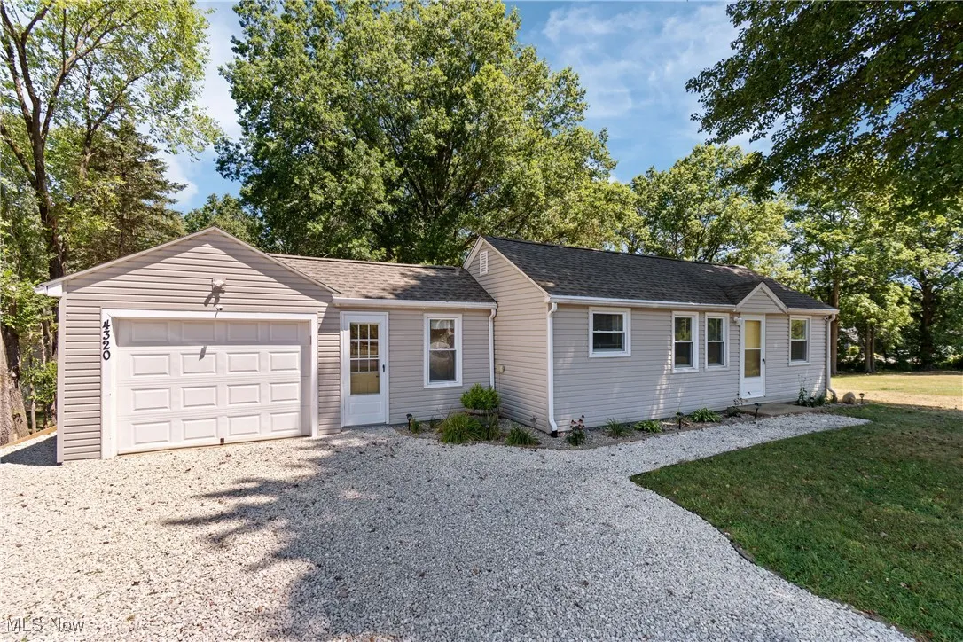 Single story home featuring an attached garage, driveway, a shingled roof, and a front lawn