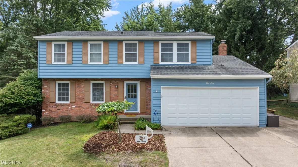 View of front facade featuring concrete driveway, a chimney, a front yard, brick siding, and an attached garage
