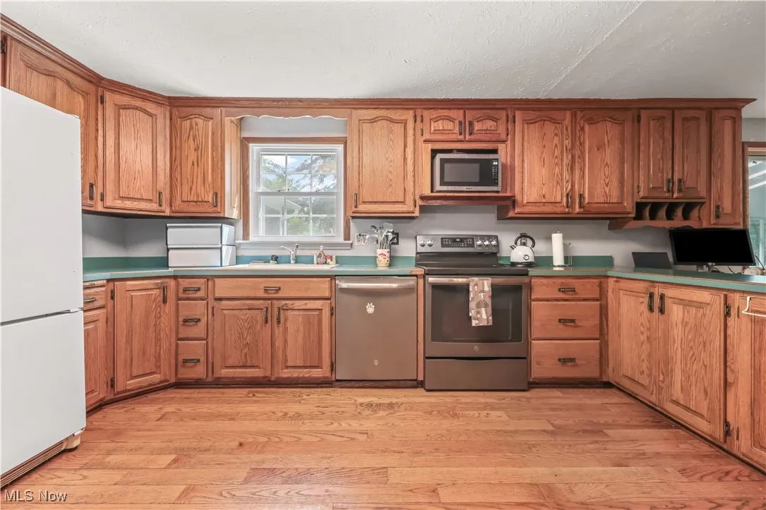 Kitchen featuring stainless steel appliances, brown cabinetry, light wood-type flooring, and a textured ceiling