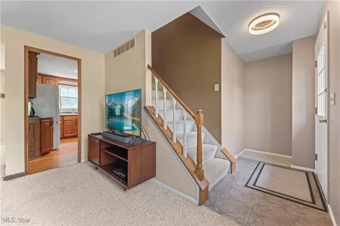Entryway with a textured ceiling, light colored carpet, and stairway