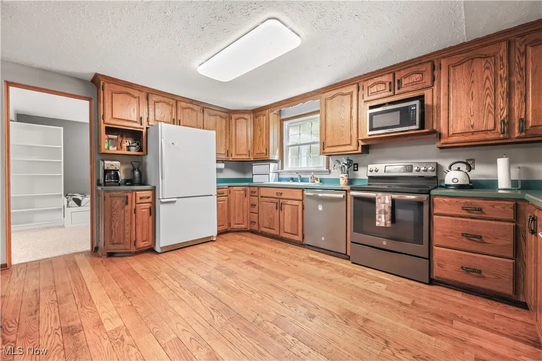 Kitchen with brown cabinets, stainless steel appliances, light wood-style floors, a textured ceiling, and open shelves