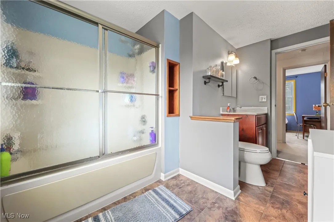 Bathroom with vanity, shower / bath combination with glass door, and a textured ceiling