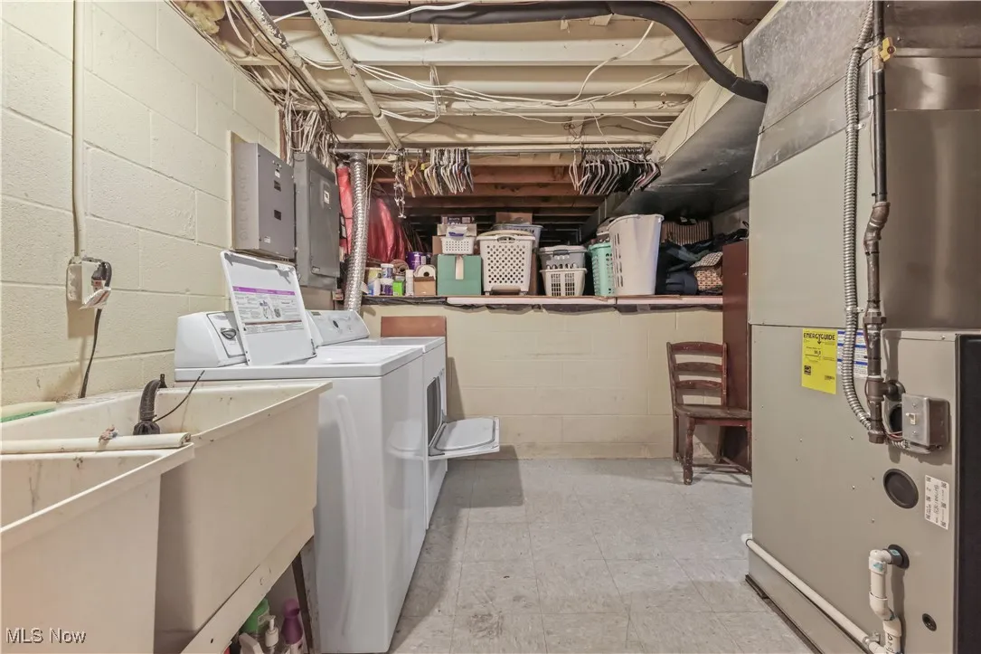 Laundry room featuring heating unit, light floors, washer and clothes dryer, and electric panel