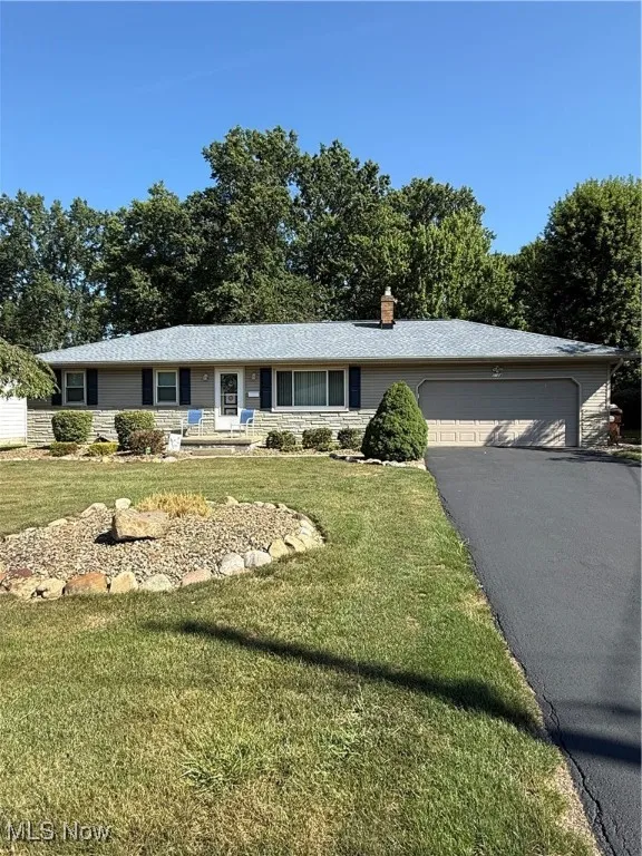 Ranch-style home featuring an attached garage, asphalt driveway, a front yard, and a chimney