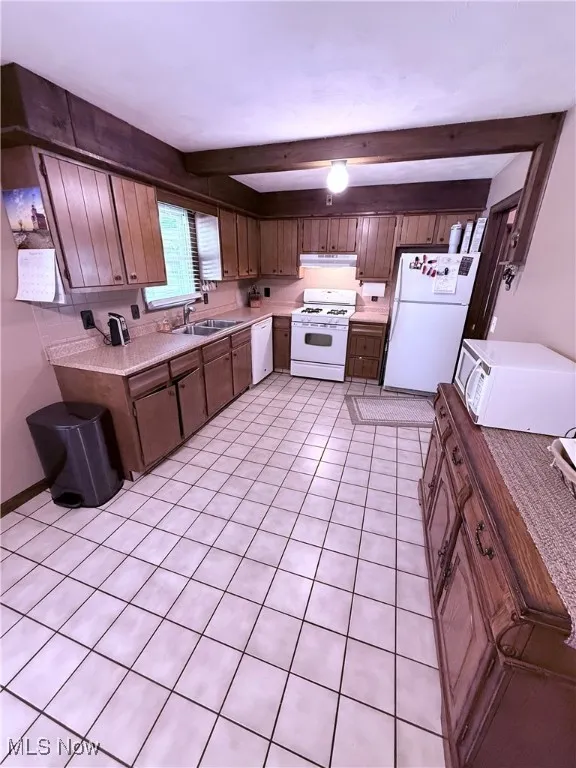 Kitchen featuring white appliances, light countertops, light tile patterned floors, beam ceiling, and under cabinet range hood