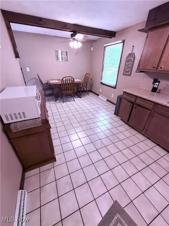 Kitchen with white microwave, light countertops, light tile patterned flooring, a ceiling fan, and beamed ceiling