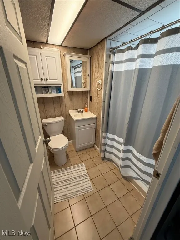 Full bath featuring light tile patterned flooring, vanity, a shower stall, wood walls, and a textured ceiling