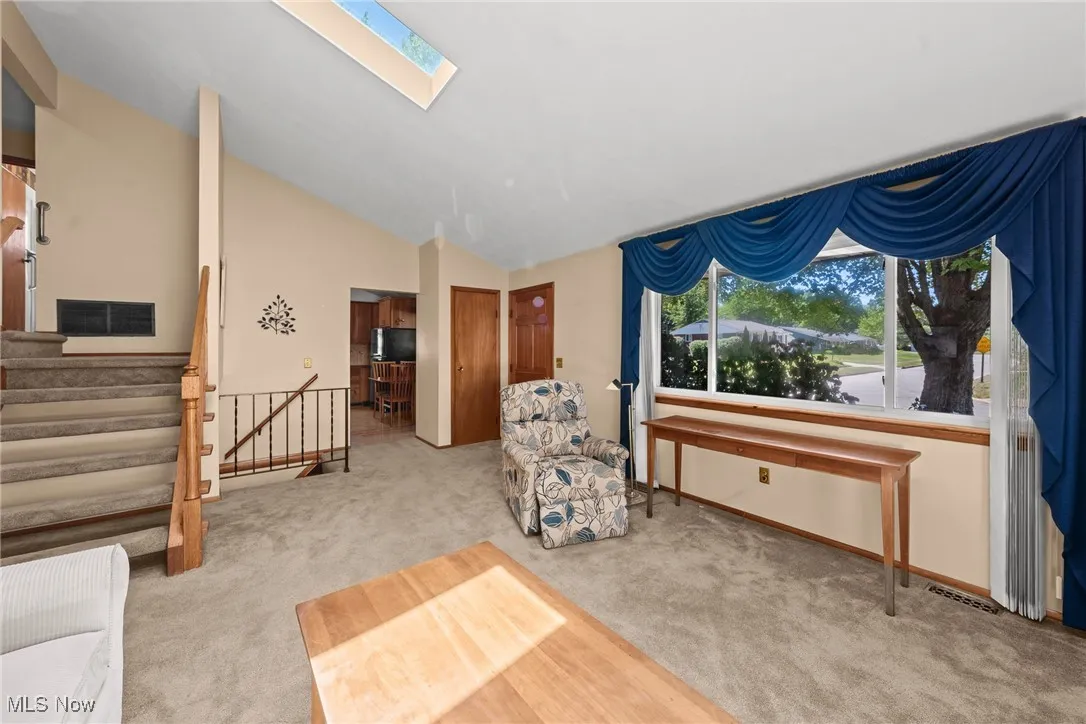Living area featuring a skylight, light carpet, lofted ceiling, and stairs