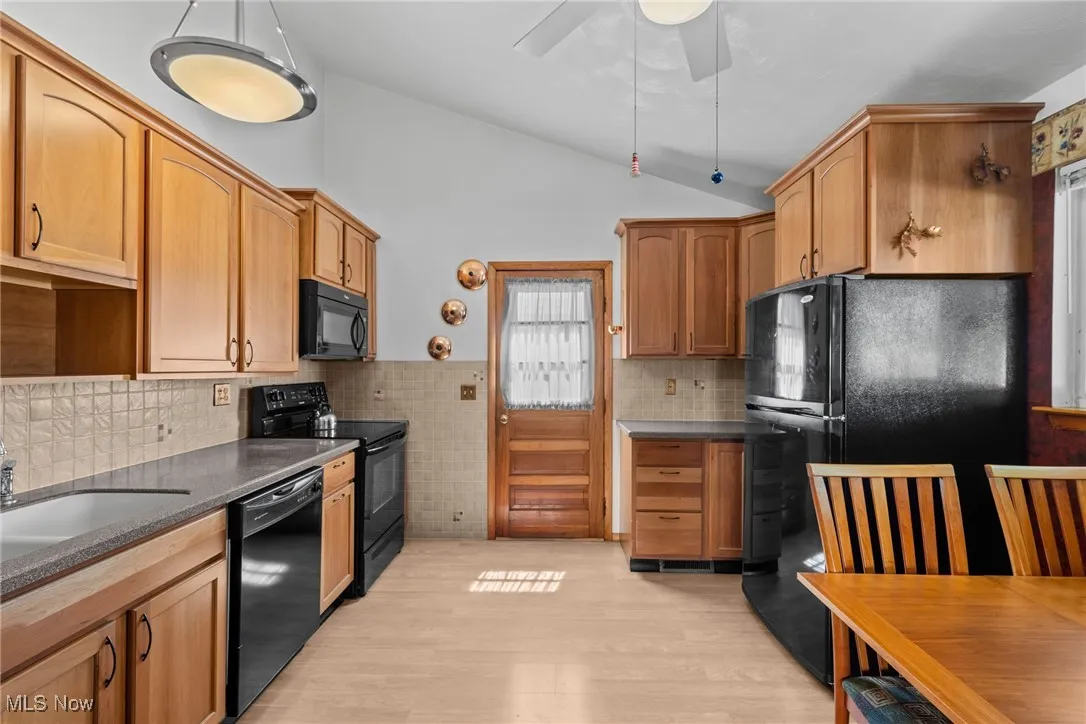 Kitchen with lofted ceiling, black appliances, light wood finished floors, decorative backsplash, and a ceiling fan