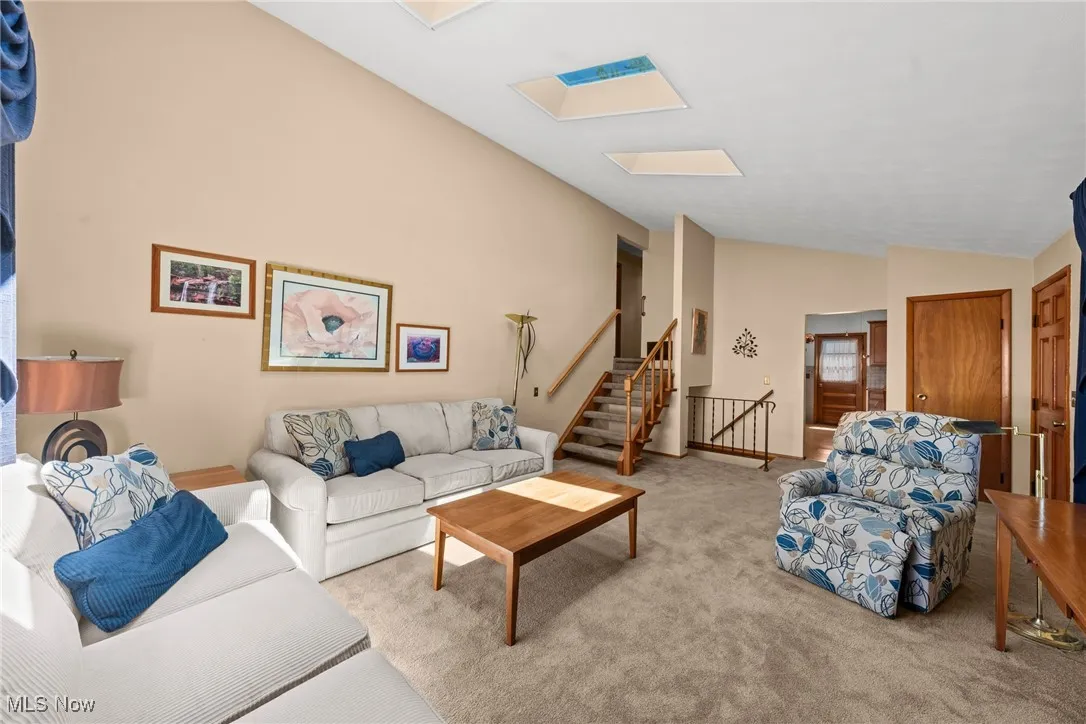 Carpeted living area featuring lofted ceiling, stairway, and a skylight