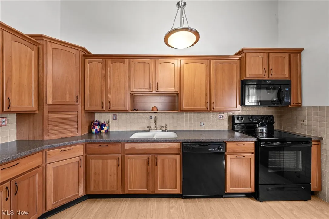 Kitchen with black appliances, light wood-style floors, backsplash, and brown cabinets