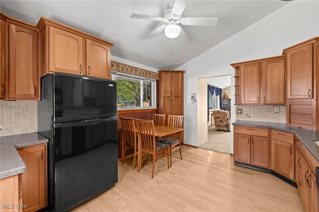 Kitchen featuring tasteful backsplash, freestanding refrigerator, lofted ceiling, open shelves, and light wood-type flooring