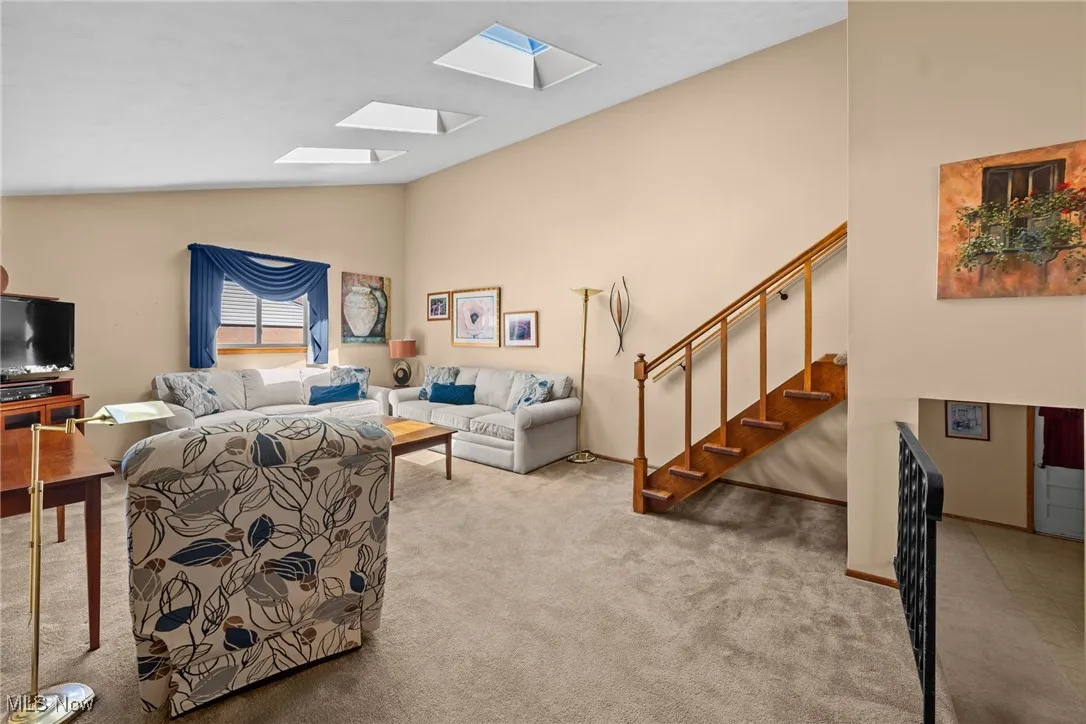 Living area featuring a skylight, stairs, light carpet, and high vaulted ceiling