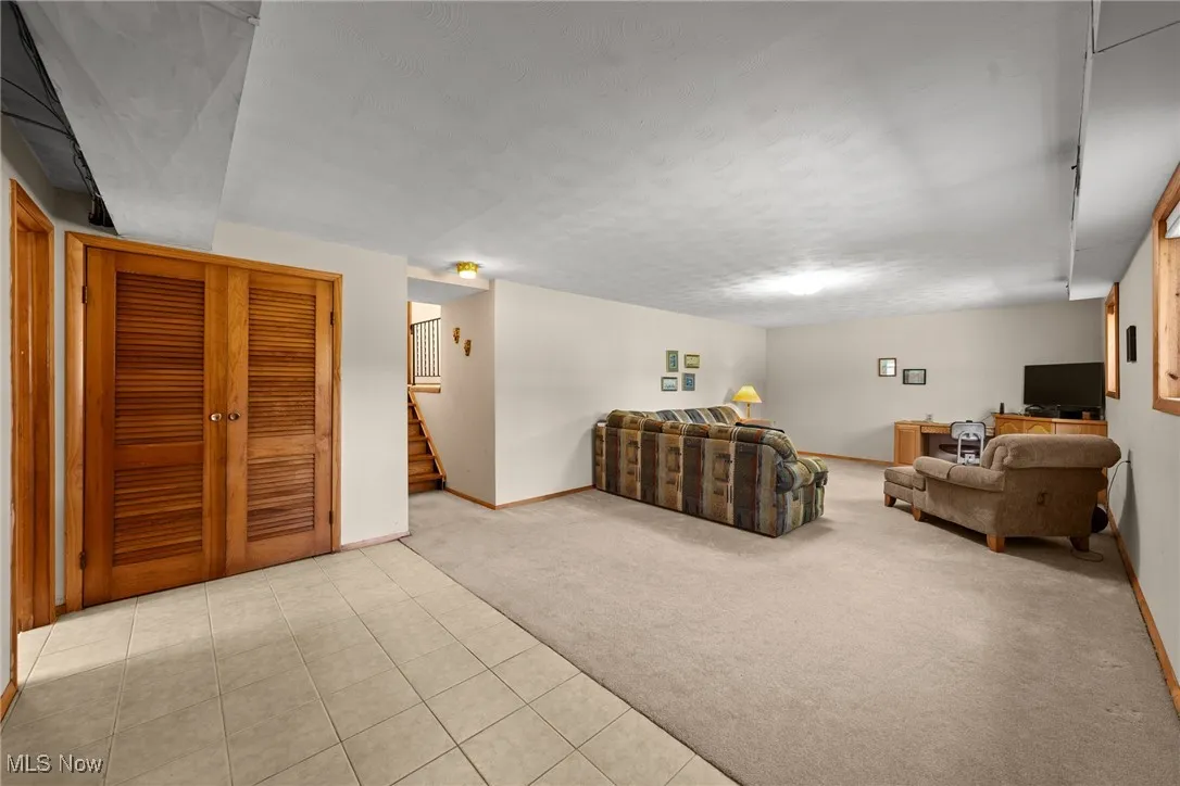 Living area featuring light colored carpet, light tile patterned flooring, and stairs