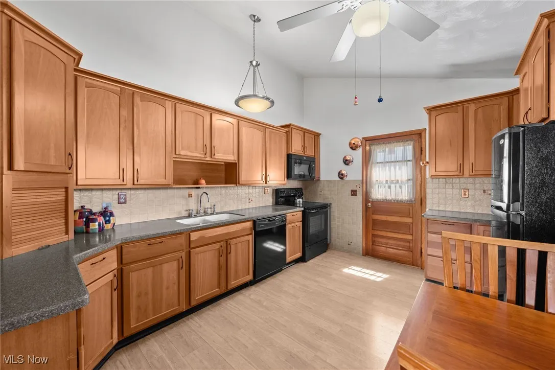 Kitchen with lofted ceiling, black appliances, light wood-style floors, decorative backsplash, and pendant lighting