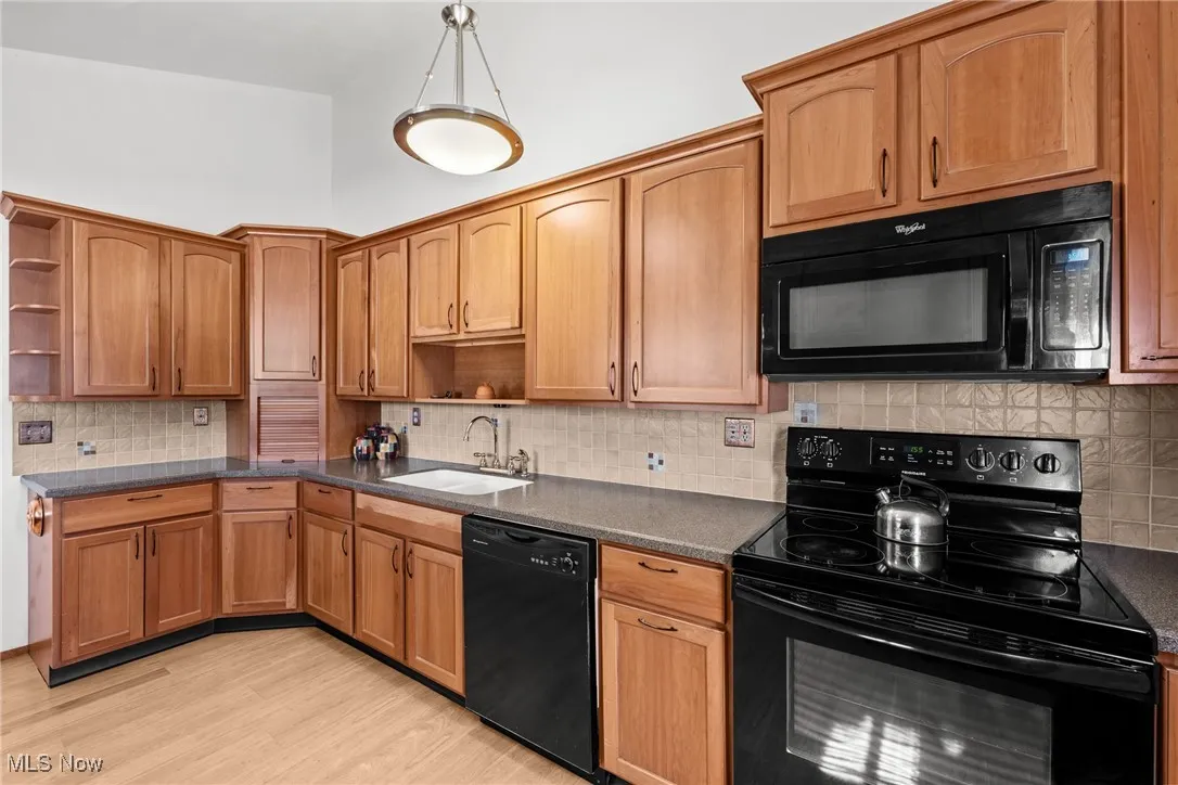 Kitchen with open shelves, black appliances, decorative backsplash, light wood-style flooring, and brown cabinets