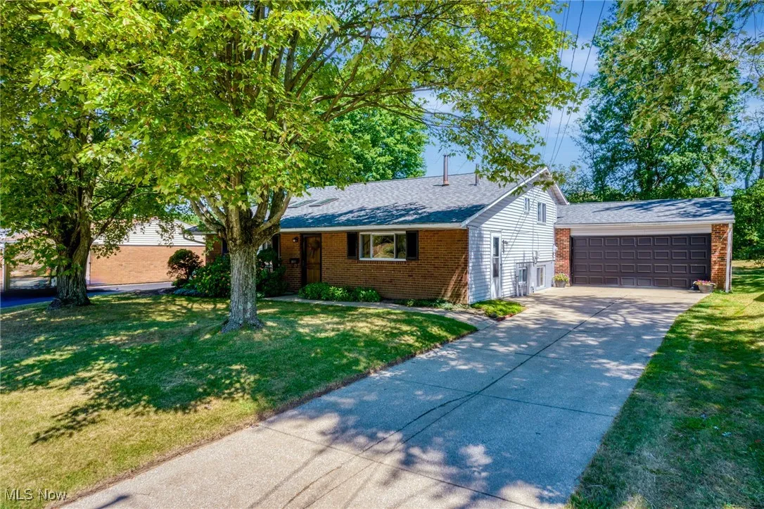 Single story home with brick siding, roof with shingles, a front yard, and concrete driveway