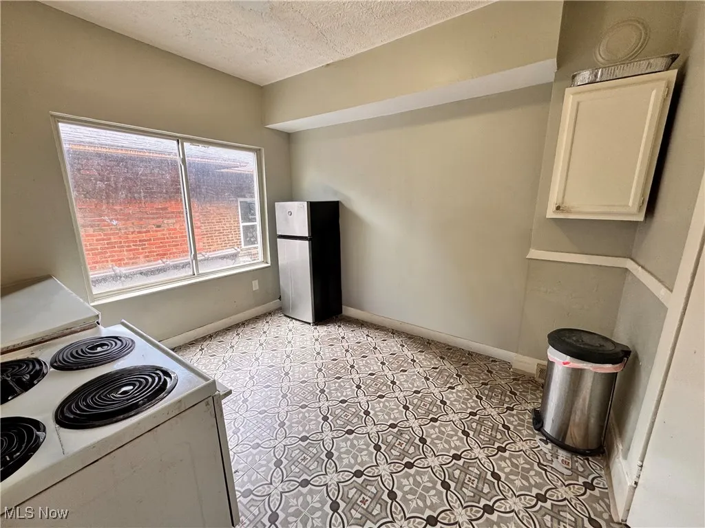 Unit 3 Kitchen with electric stove, a textured ceiling, freestanding refrigerator, and white cabinetry