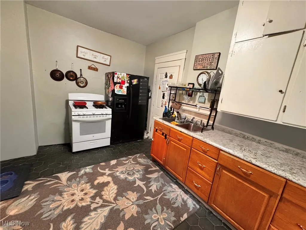 Unit 2 Kitchen with white gas range oven, black fridge with ice dispenser, dark tile patterned floors, light countertops, and brown cabinetry