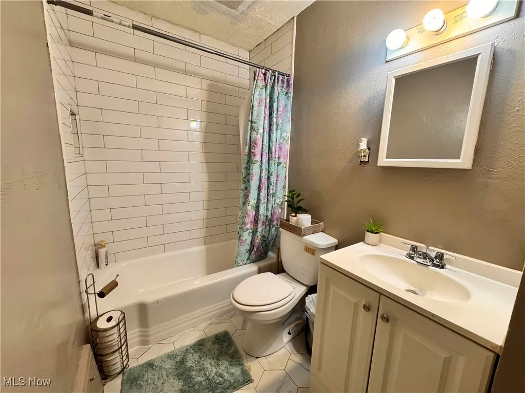 Unit 1 Full bathroom with shower / tub combo with curtain, vanity, light tile patterned floors, a textured ceiling, and a textured wall