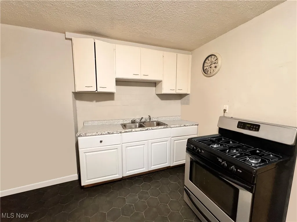 Unit 1 Kitchen with stainless steel range with gas stovetop, a textured ceiling, white cabinetry, light countertops, and backsplash