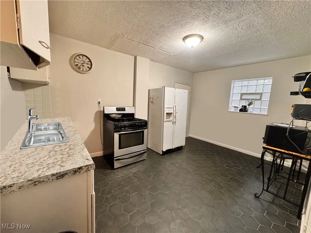 UNIT 1 Kitchen featuring light countertops, stainless steel gas stove, white refrigerator with ice dispenser, white cabinets, and a textured ceiling