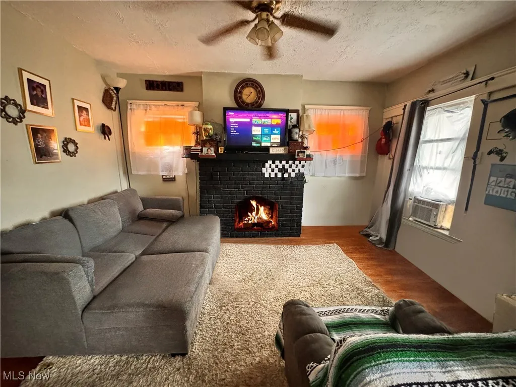 Unit 2 Living room with wood finished floors, a textured ceiling, a brick fireplace, and a ceiling fan