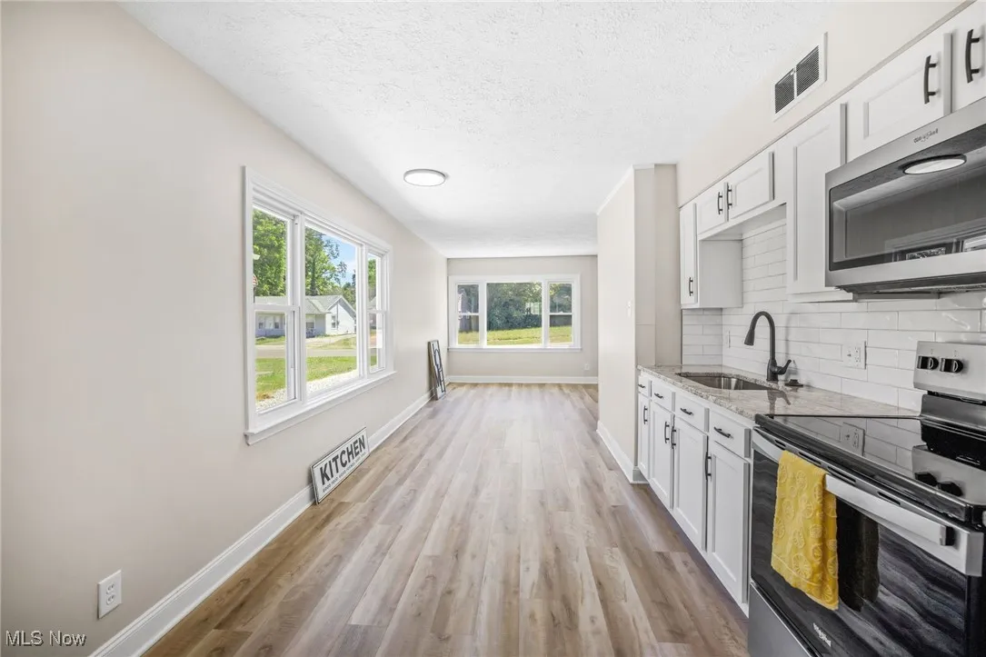 Kitchen with appliances with stainless steel finishes, light stone counters, white cabinetry, light wood-style flooring, and a textured ceiling
