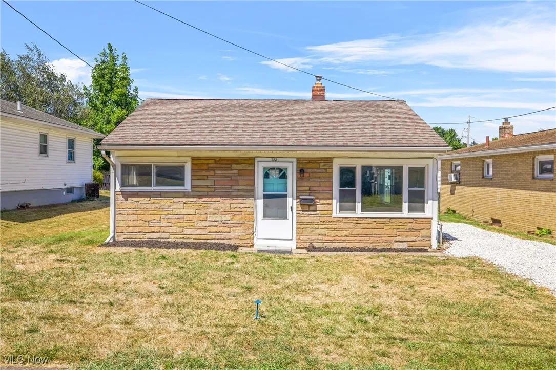 View of front facade featuring roof with shingles, stone siding, and a front yard