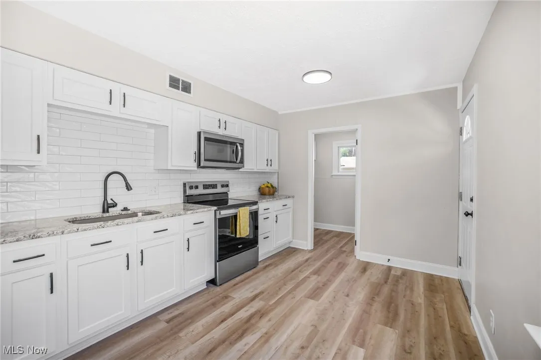 Kitchen with appliances with stainless steel finishes, white cabinetry, decorative backsplash, light wood finished floors, and light stone counters