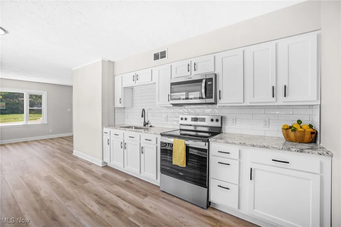 Kitchen featuring stainless steel appliances, white cabinets, light stone countertops, decorative backsplash, and a textured ceiling
