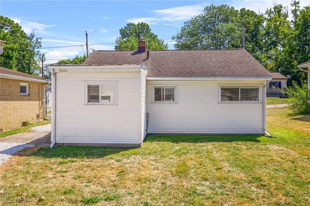 Back of property with a yard, a shingled roof, and a chimney