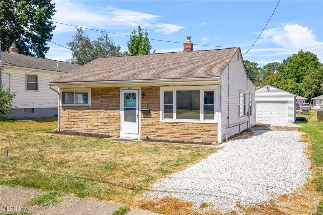 View of front of property with roof with shingles, stone siding, a front lawn, driveway, and a chimney
