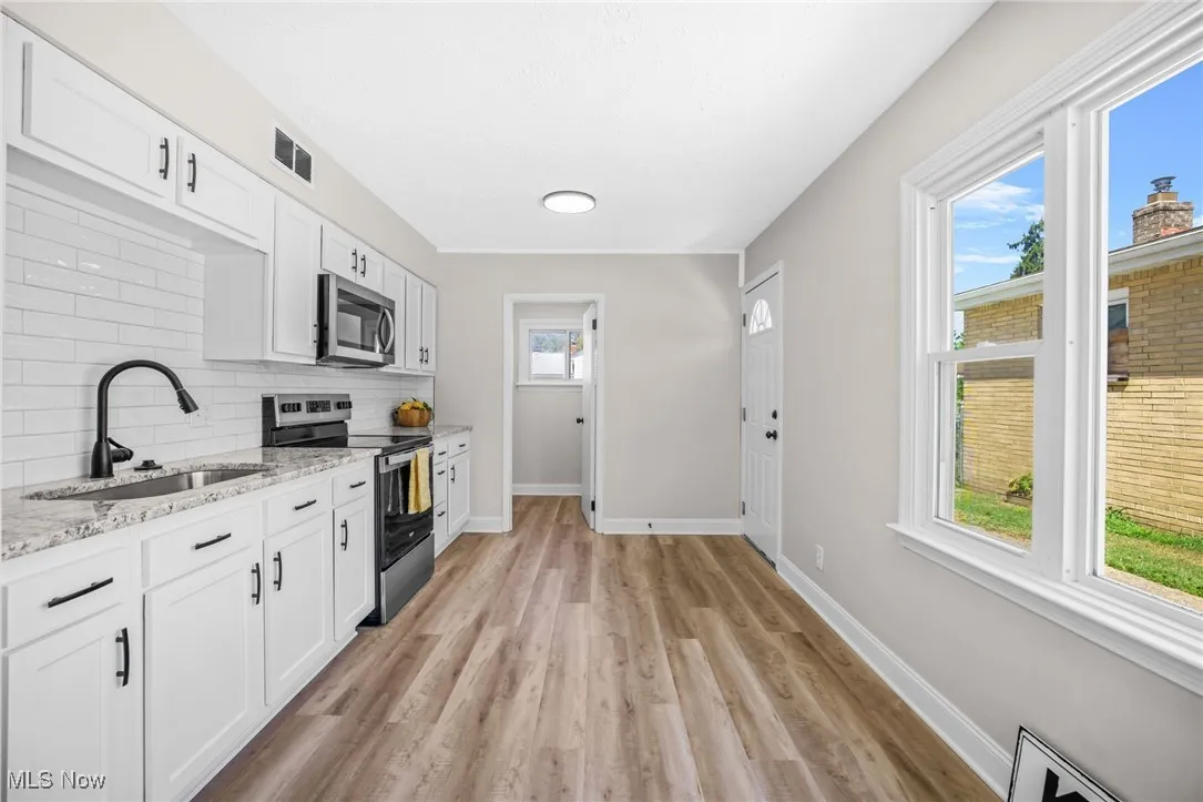 Kitchen featuring appliances with stainless steel finishes, white cabinetry, light stone countertops, and light wood-style floors
