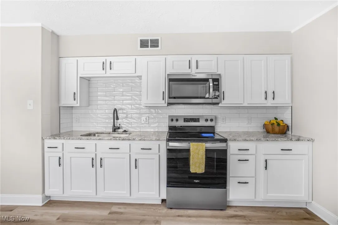 Kitchen with appliances with stainless steel finishes, white cabinetry, light stone countertops, light wood-style flooring, and backsplash
