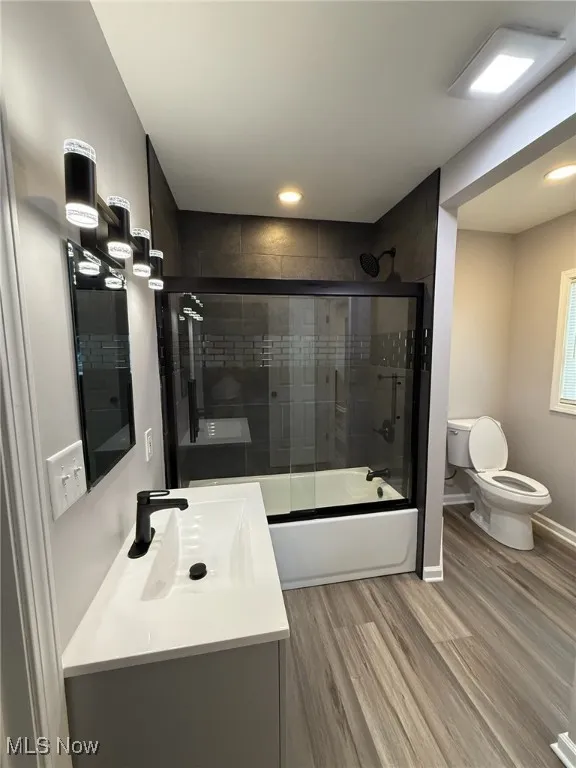 Full bath with combined bath / shower with glass door, vanity, and light wood finished floors