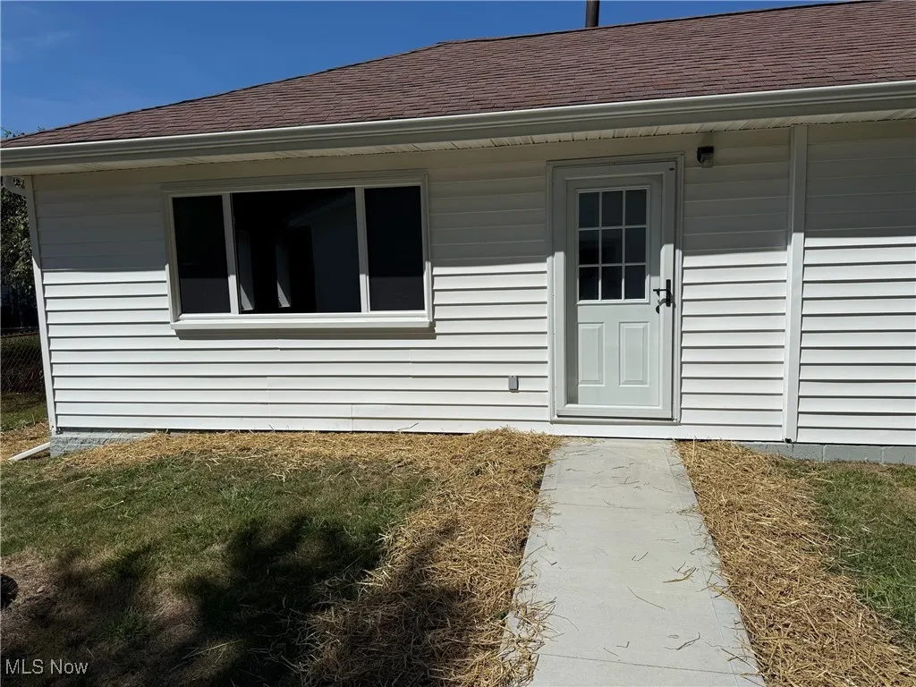 Entrance to property with a shingled roof and a lawn