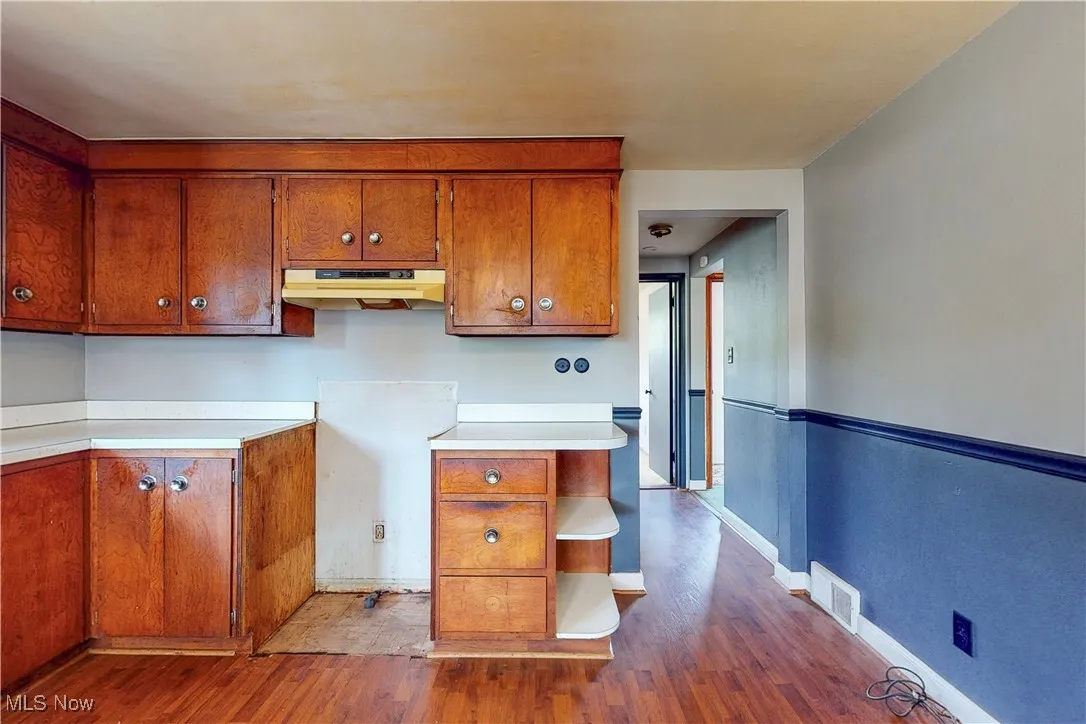 Kitchen with light countertops, brown cabinets, dark wood-style flooring, and under cabinet range hood