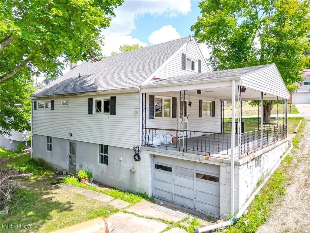 Back of house featuring a shingled roof, a chimney, a porch, and an attached garage