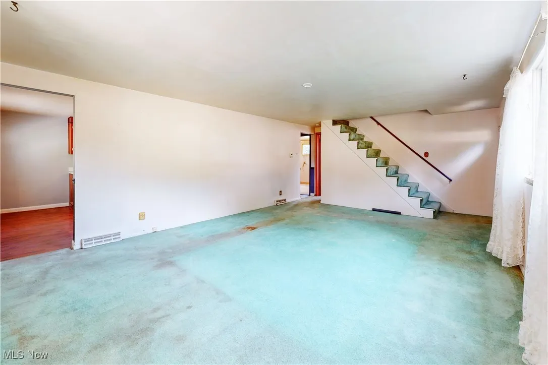 Unfurnished living room featuring carpet flooring and stairs