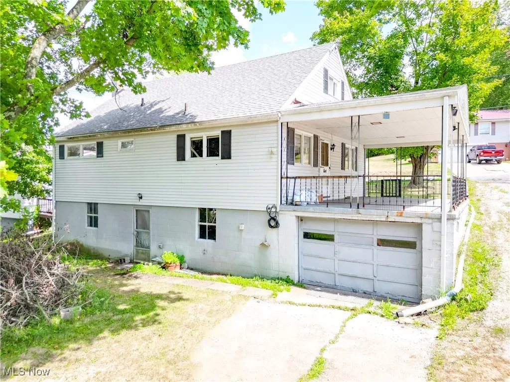 Rear view of property featuring a shingled roof, an attached garage, and driveway