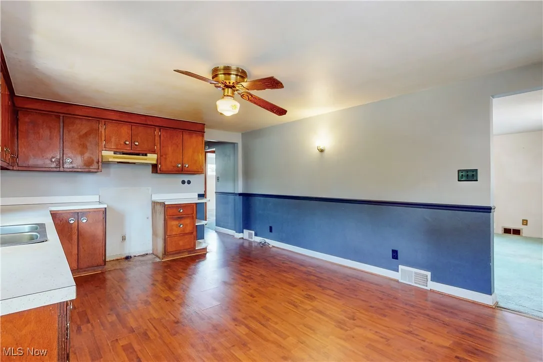 Kitchen featuring light countertops, dark wood-style flooring, ceiling fan, and brown cabinets