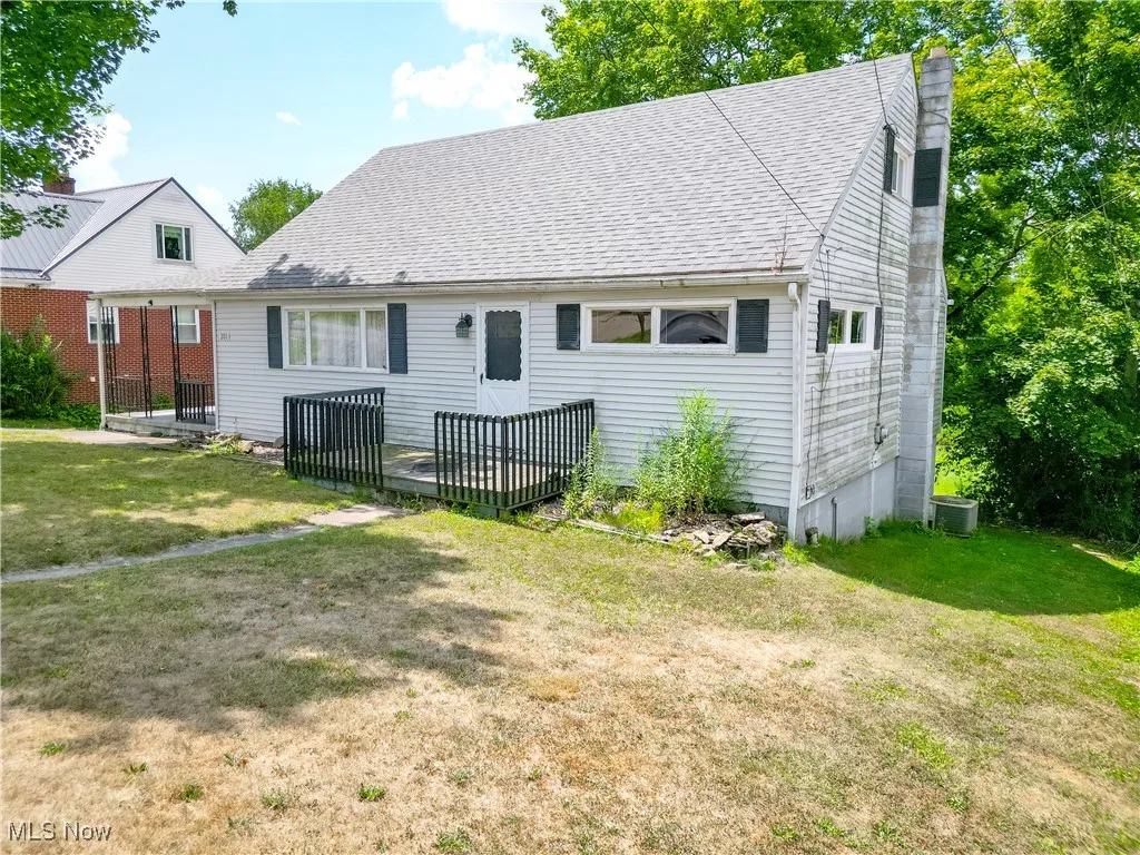 Rear view of house featuring a yard, a shingled roof, and a chimney