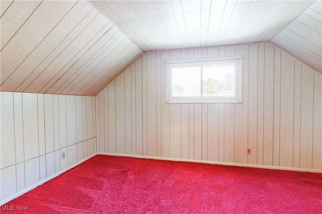Bonus room with lofted ceiling, wood walls, and carpet floors