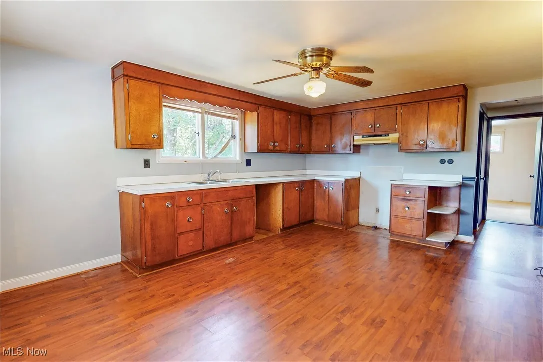 Kitchen featuring light countertops, brown cabinetry, dark wood-style flooring, ceiling fan, and under cabinet range hood